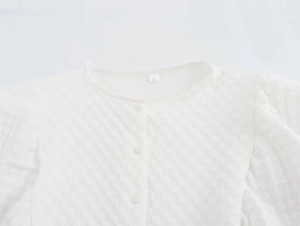 Detail of white puff sleeve dress featuring checkered texture fabric and fabric-covered buttons