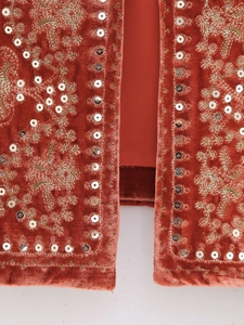 Macro shot of rust red velvet vest featuring floral embroidery and silver sequins