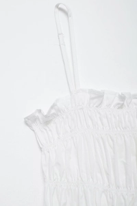 Detail of adjustable spaghetti straps and ruffled smocking on white summer dress