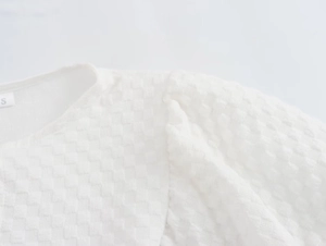 Detail of white puff sleeve top featuring textured grid fabric and inner size S tag