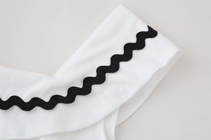 Detailed close-up of white cotton linen fabric with decorative black rickrack wave trim