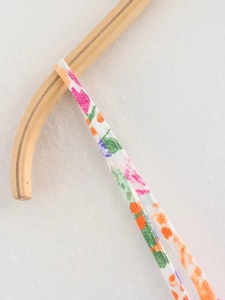 Close-up of thin shoulder straps with colorful floral print hanging on a wooden hanger