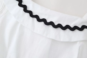 Detailed view of white cotton top featuring black ric-rac trim on wide collar design