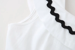 Detail of white cotton linen dress showing black rick-rack wave trim on the shoulder