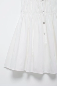 Close-up of white dress with smocked elastic waist and decorative shell buttons