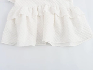 Detailed close-up of white dress with plaid jacquard fabric and tiered ruffle edges