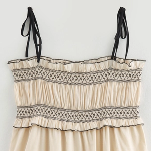 Elegant beige smocked midi dress with black geometric embroidery and thin tie straps
