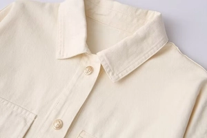 Detail of a beige twill jacket showing the lapel and embossed gold metal button