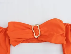 Detail of orange tube top featuring a gold metal buckle and pleated fabric texture