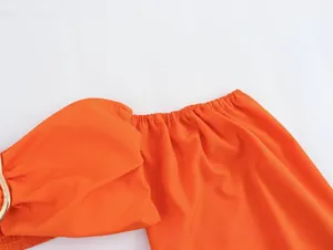 Detail of orange off-shoulder top with elastic neckline and gold metal ring accents