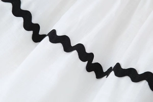 Detail of white cotton linen fabric featuring contrast black rick-rack wave lace trim