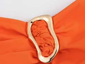 Detail of a bright orange fabric top featuring a stylish irregular gold metal buckle
