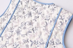 Detail shot of vintage floral print vest with diamond quilting and light blue piping edge