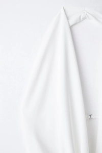 Detail of white halter dress featuring a smooth fabric texture and silver J-shaped metal buckle