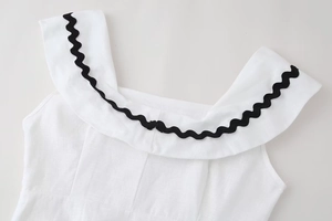 Detail view of white linen dress neckline with black rickrack wave trim and ruffles