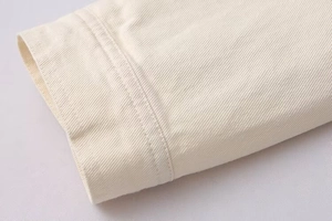 Close-up of cream cotton jacket showing textured twill fabric and double-stitched seams