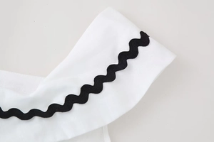 Close-up of white cotton linen dress detail with contrast black rickrack wavy trim edges