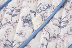 Close-up of quilted floral puffer vest featuring diamond stitching and blue edge piping detail
