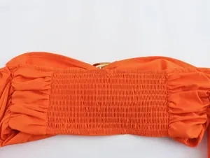 Close-up of orange smocked tube top detail with golden metal ring hardware and fine texture