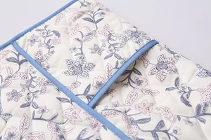 Detail of quilted vest fabric with floral prints and contrast blue piping finish