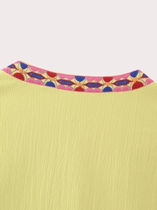 Gros plan détaillé sur la broderie géométrique du col de ce gilet ethnique jaune
