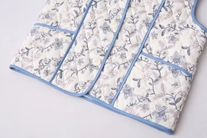 Detailed view of white quilted vest featuring blue floral print and light blue piping finish