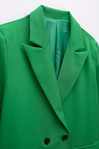 Detailed close-up of peak lapel and black buttons on a bright green woven blazer jacket