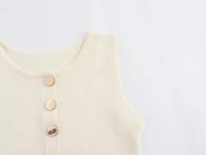 Detailed close-up of cream knit top featuring three polished gold buttons on the chest