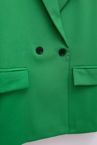 Detail view of a bright green double-breasted blazer showing black buttons and flap pockets