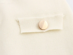 Detail of high-quality cream knit dress featuring a pocket flap and large gold metal button
