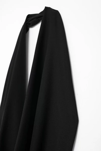 Detail of elegant black halter dress featuring a knotted neckline and smooth draped fabric