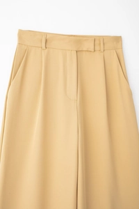 Détail d'un pantalon large plissé à taille haute jaune moutarde en tissu tissé texturé