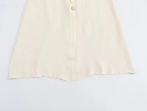 Close-up of cream knit dress featuring fine ribbed texture and decorative gold buttons