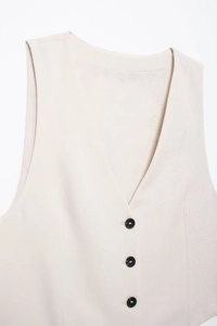 Detailed view of women's linen vest v-neckline with contrasting black buttons and textured fabric