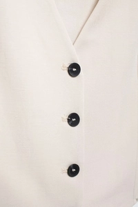 Detail of V-neck beige linen vest featuring three black contrast buttons and fabric texture