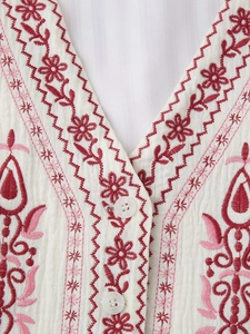 Detail of V-neck white vest featuring delicate red floral embroidery and pearly buttons