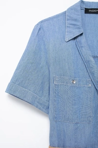 Detail of light blue denim midi dress showing pointed collar, sleeve, and metal button pocket