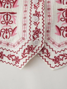 Close-up of floral embroidery and white buttons on ivory textured V-neck vest
