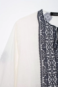 Detail of white linen blouse with black paisley patterns and decorative neck ties