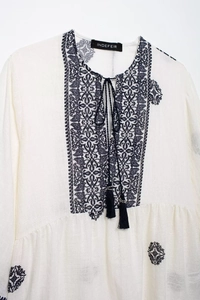 Detailed close-up of ethnic blue embroidery and tassel ties on a beige linen shirt