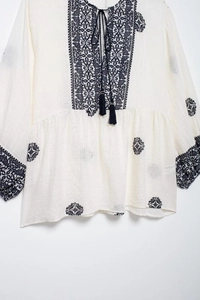 Detail of bohemian ivory blouse featuring V-neck ties and blue Paisley floral embroidery