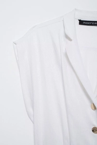 Détail du col d'une chemise sans manches en lin blanc avec boutons dorés et revers