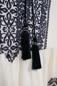 Detail of bohemian white blouse with navy blue geometric embroidery and tasseled ties