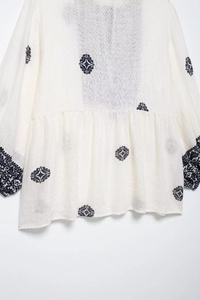 Detailed close-up of blue geometric floral embroidery on a white bohemian cotton linen shirt