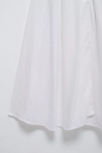 Gros plan de l'ourlet de la robe chemise blanche montrant la texture fine du coton