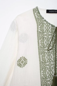 Close-up of white linen shirt featuring green paisley embroidery and boho tassel drawstrings