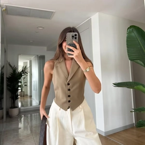 Detail of tailored khaki vest with five buttons and sharp triangular hemline