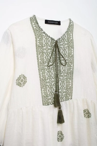 Detail of ethnic green embroidery and V-neck tassel drawstring on boho cream shirt