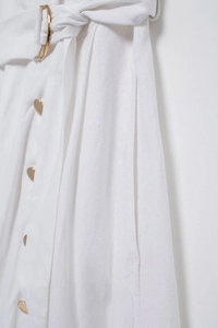 Détail d'une robe blanche en coton avec boutons dorés ronds et taille ceinturée assortie