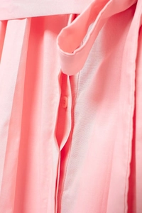 Detail of pink pleated shirt dress featuring waist belt and tonal button on cotton fabric